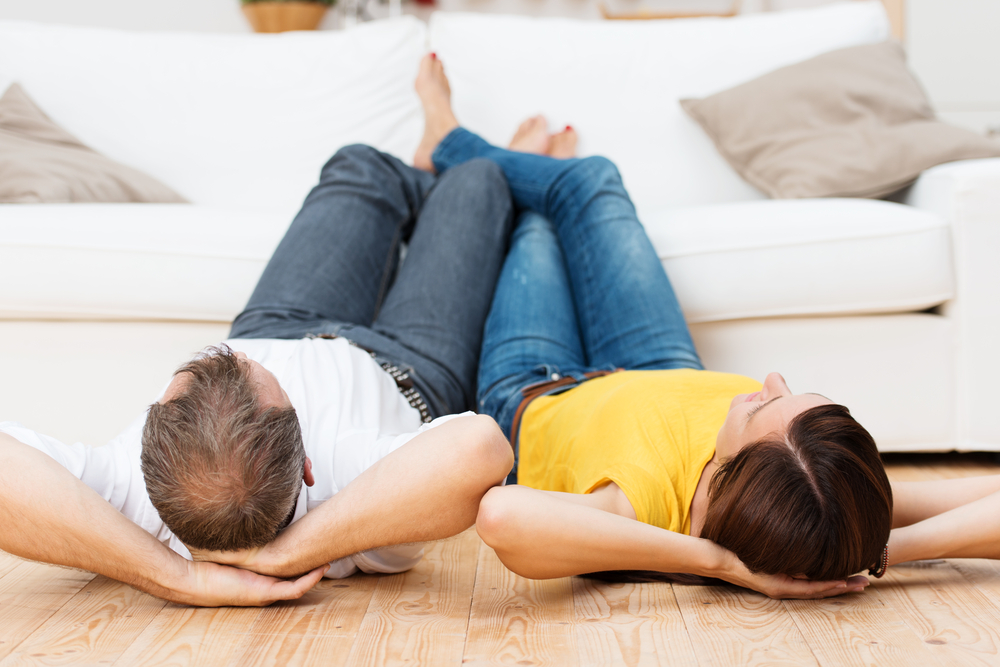 Young couple sharing a relaxing day lying side by side on their backs on a wooden living room floor with their bare feet up on the sofa Young couple sharing a relaxing day lying side by side on their backs on a wooden living room floor with their bare feet up on the sofa
